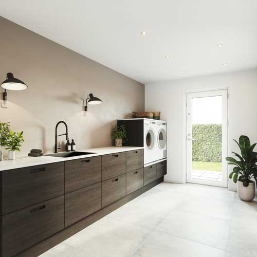 Finerfronter i bryggerset med hævet vaskemaskine og tørretumbler. Bordpladen er i hvid laminat med en integreret silgranitvask. Fronterne er stilrene med vandret vild egetræsfiner og indfræsede, firkantede greb. Bryggerset er rummeligt og brugervenligt.