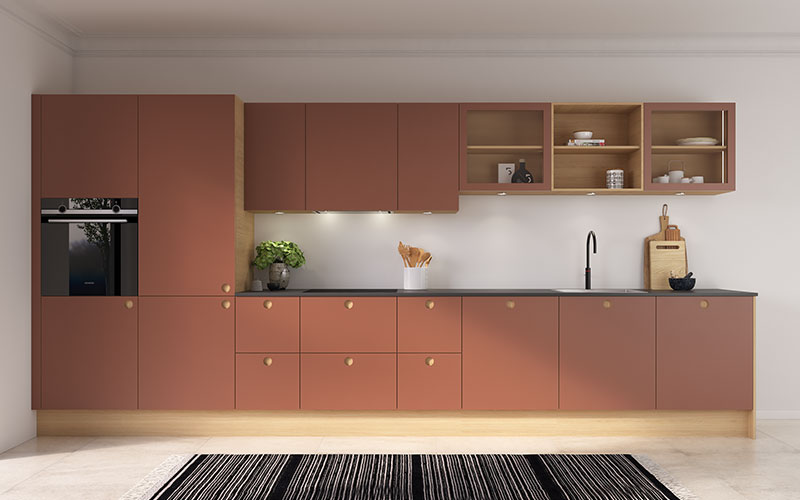 Køkkenets fronter er udført i tidløst linoleum med massive egetræskanter, hvilket skaber et varmt, moderne og modigt udtryk. Det er et fleksibelt køkken, der passer perfekt både til sommerhuset og den mindre lejlighed – ideelt til dem, der ønsker et enkelt, funktionelt og personligt design. Fronterne består af 22 mm plader med linoleum i farven 4008 Brick, her vist med indfræset greb i modellen C-Line, som giver et elegant og strømlinet look. Overskabene er designet uden greb og åbnes via push-funktion, hvilket understreger det rene og moderne udtryk. Bag de harmoniske fronter er både køleskab og opvaskemaskine skjult, og emhætten er diskret integreret i overskabet, så den fremstår næsten usynlig. De åbne reoler i vandret egetræsfiner tilfører varme og naturlig struktur til rummet.